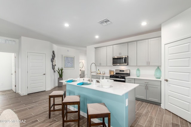 kitchen featuring a breakfast bar area, gray cabinets, a kitchen island with sink, and appliances with stainless steel finishes