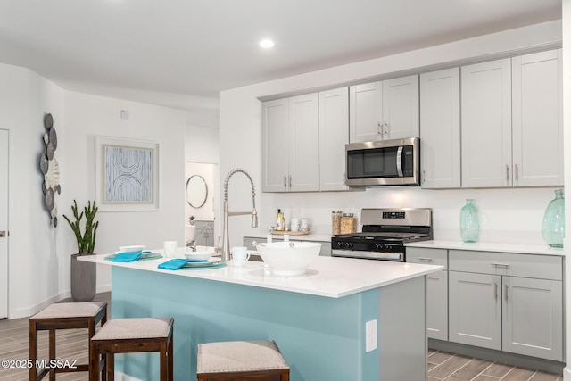 kitchen featuring a kitchen bar, gray cabinetry, a center island with sink, and stainless steel appliances