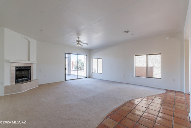 unfurnished living room featuring a tiled fireplace, ceiling fan, and carpet floors