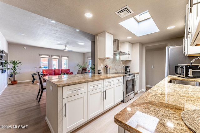 kitchen with stainless steel range with electric cooktop, white cabinets, wall chimney range hood, sink, and light stone countertops