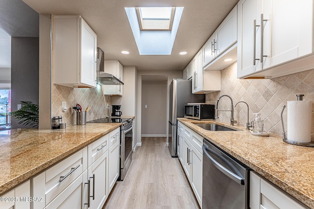 kitchen with a skylight, white cabinetry, sink, light stone counters, and appliances with stainless steel finishes