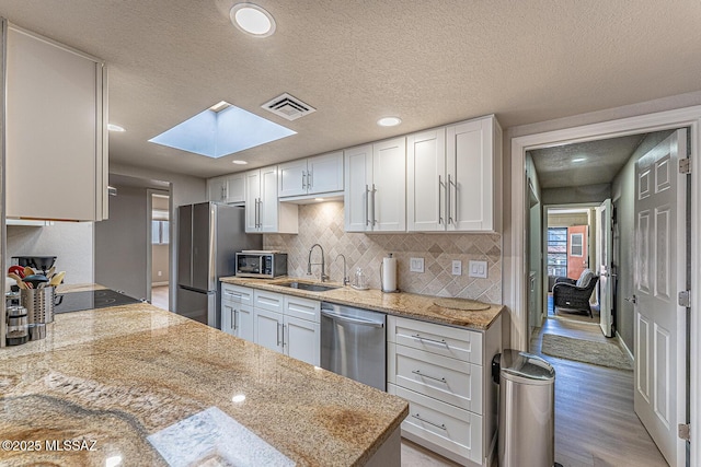 kitchen with white cabinets, sink, appliances with stainless steel finishes, and a skylight