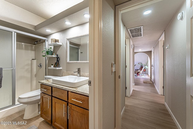 bathroom with a textured ceiling, vanity, a shower with door, hardwood / wood-style flooring, and toilet