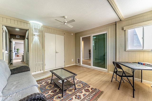 living room with ceiling fan, light hardwood / wood-style flooring, and wood walls