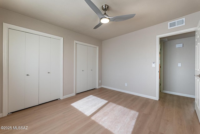 unfurnished bedroom with ceiling fan, light hardwood / wood-style floors, and two closets