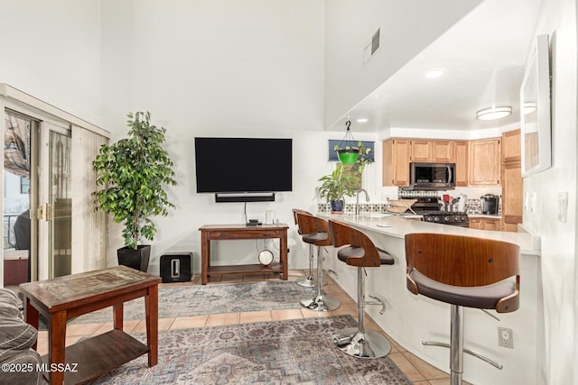 kitchen featuring kitchen peninsula, light tile patterned flooring, appliances with stainless steel finishes, a kitchen breakfast bar, and light brown cabinetry