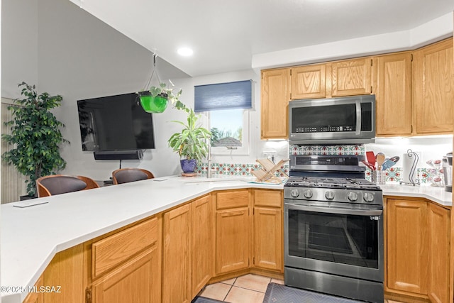 kitchen with stainless steel appliances, light countertops, a peninsula, and light tile patterned floors