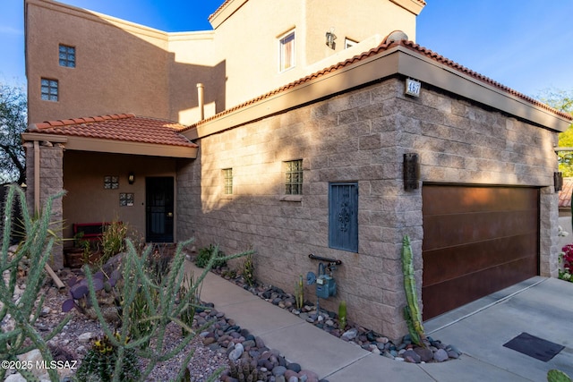 view of side of home with a garage, concrete driveway, a tiled roof, and stucco siding