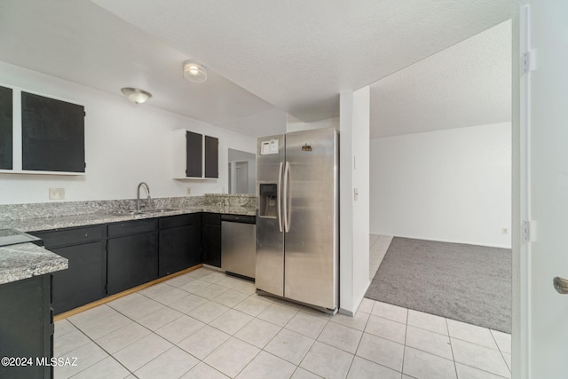 kitchen with sink, light stone counters, a textured ceiling, light carpet, and appliances with stainless steel finishes