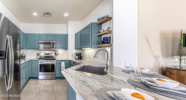 kitchen with light stone countertops, appliances with stainless steel finishes, backsplash, blue cabinets, and sink