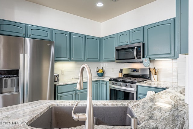 kitchen with decorative backsplash, appliances with stainless steel finishes, light stone countertops, blue cabinets, and sink