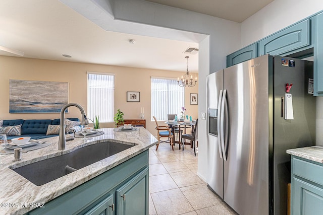 kitchen with an inviting chandelier, sink, stainless steel refrigerator with ice dispenser, light stone countertops, and light tile patterned floors