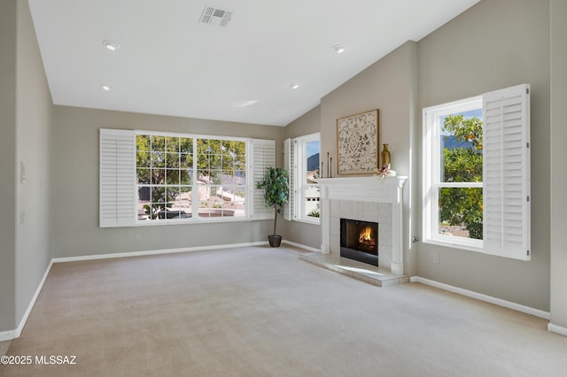 unfurnished living room featuring light colored carpet, vaulted ceiling, a wealth of natural light, and a tiled fireplace