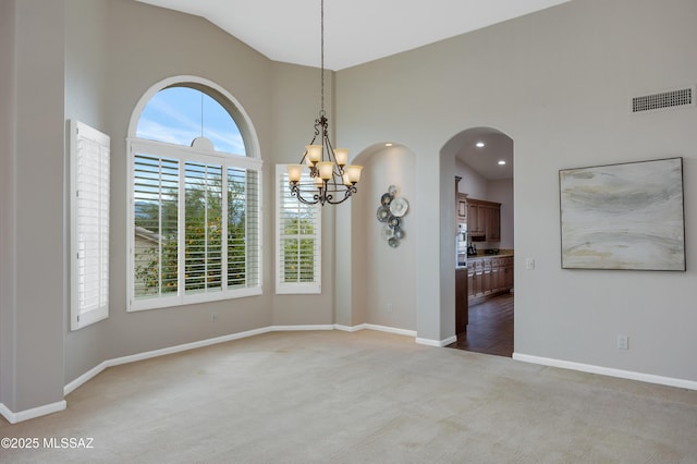 carpeted spare room with high vaulted ceiling and an inviting chandelier