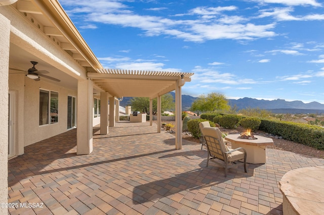 view of patio with ceiling fan, an outdoor fire pit, a pergola, and a mountain view