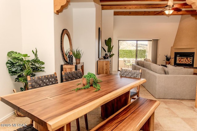 dining area featuring ceiling fan, a large fireplace, and beamed ceiling