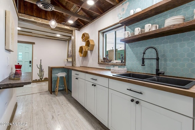 kitchen featuring wooden counters, light wood-type flooring, sink, wooden ceiling, and white cabinets