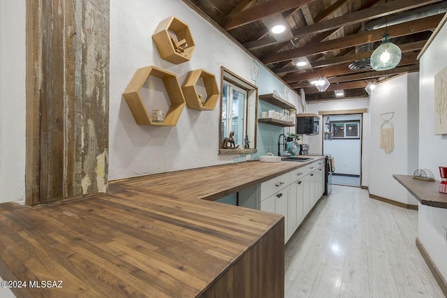 kitchen with wooden counters, light wood-type flooring, sink, decorative light fixtures, and white cabinets