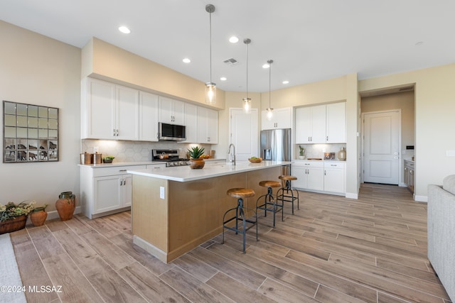 kitchen with decorative backsplash, appliances with stainless steel finishes, a kitchen island with sink, white cabinetry, and hanging light fixtures