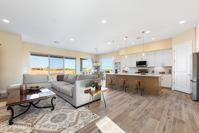 living room with an inviting chandelier, sink, and light hardwood / wood-style flooring