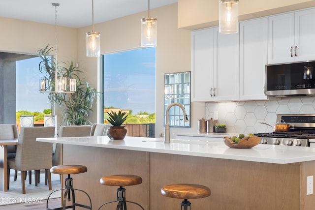 kitchen featuring appliances with stainless steel finishes, tasteful backsplash, decorative light fixtures, white cabinets, and a breakfast bar area