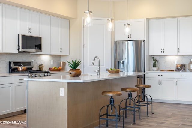 kitchen featuring a center island with sink, decorative light fixtures, white cabinetry, and stainless steel appliances