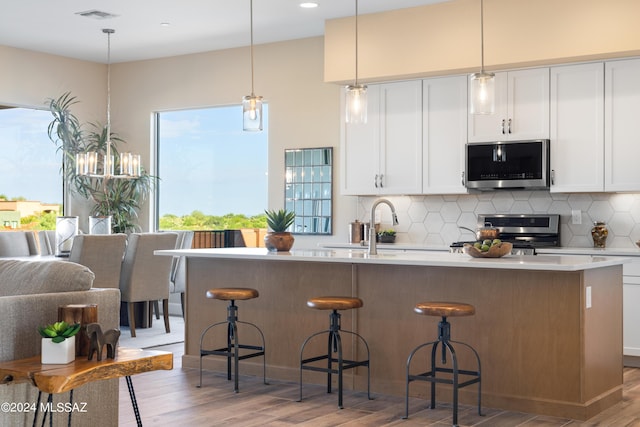 kitchen with pendant lighting, white cabinets, a kitchen island with sink, and appliances with stainless steel finishes