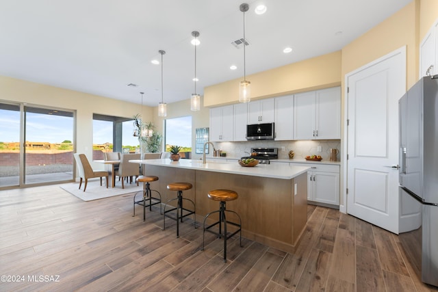 kitchen with appliances with stainless steel finishes, a center island with sink, and white cabinetry