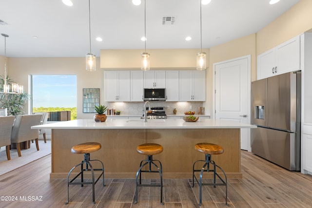 kitchen with white cabinetry, a kitchen island with sink, stainless steel appliances, and decorative light fixtures