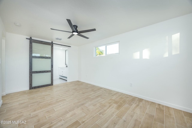 empty room with a barn door, ceiling fan, and light hardwood / wood-style flooring