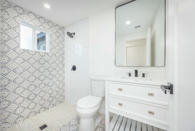 bathroom with toilet, a tile shower, and vanity