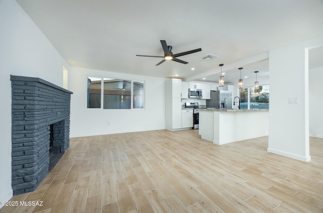 unfurnished living room featuring ceiling fan, sink, a fireplace, and light hardwood / wood-style flooring