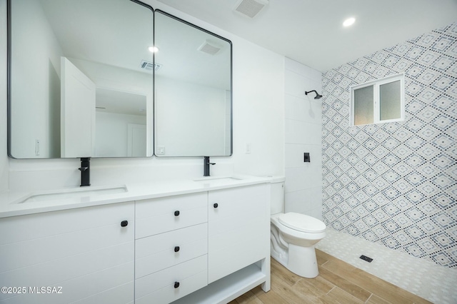 bathroom with a tile shower, vanity, and toilet