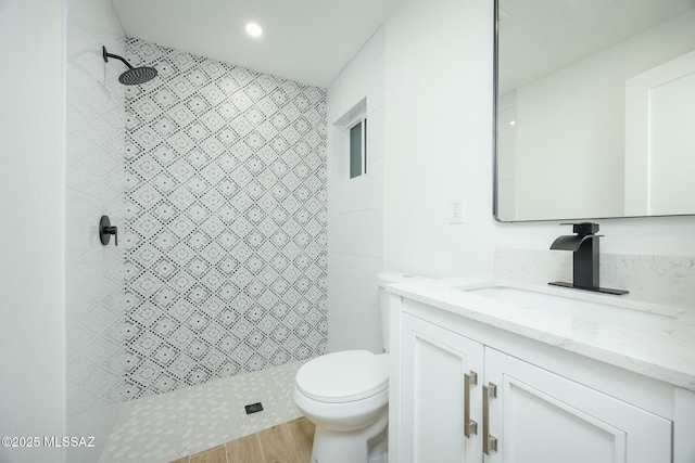 bathroom featuring a tile shower, hardwood / wood-style floors, vanity, and toilet