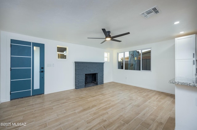 unfurnished living room with light wood-type flooring, a stone fireplace, and ceiling fan