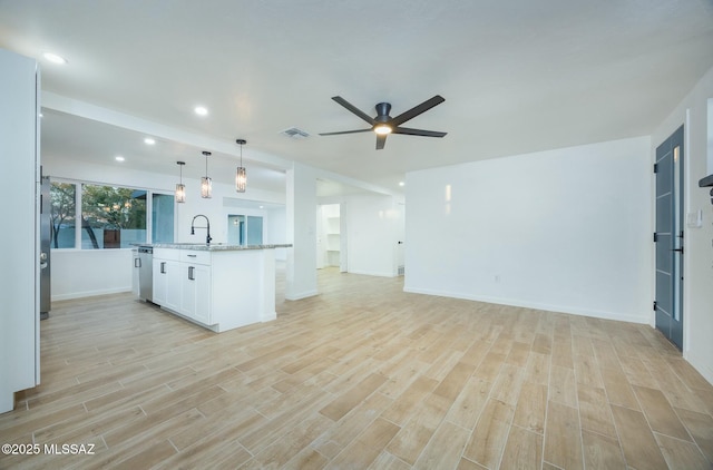 kitchen featuring light stone counters, a kitchen island with sink, sink, white cabinets, and hanging light fixtures