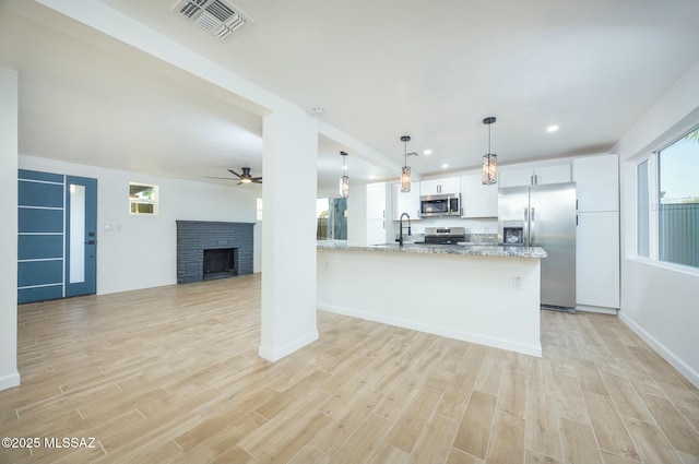 kitchen with light stone countertops, appliances with stainless steel finishes, kitchen peninsula, decorative light fixtures, and white cabinetry