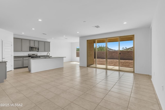 kitchen with gray cabinetry, a center island with sink, light tile patterned floors, and stainless steel appliances