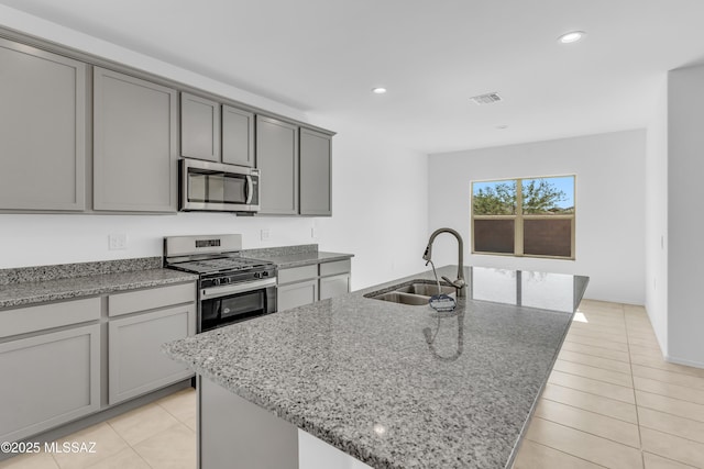 kitchen featuring stone counters, a center island with sink, sink, gas range, and light tile patterned floors