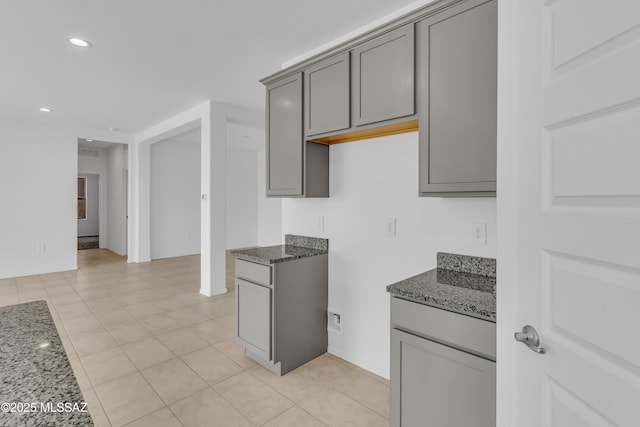 kitchen featuring gray cabinets, light tile patterned flooring, and dark stone counters