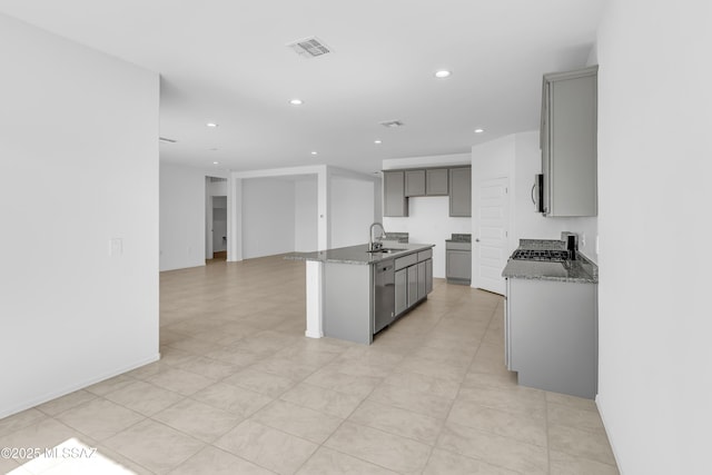 kitchen featuring gray cabinetry, sink, dark stone countertops, an island with sink, and stainless steel appliances