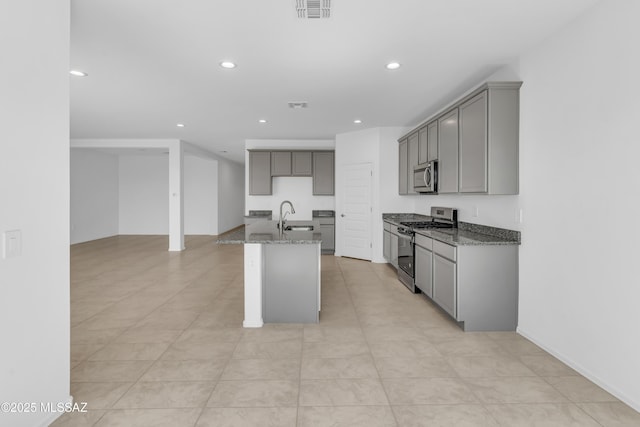 kitchen featuring sink, an island with sink, dark stone counters, gray cabinets, and appliances with stainless steel finishes