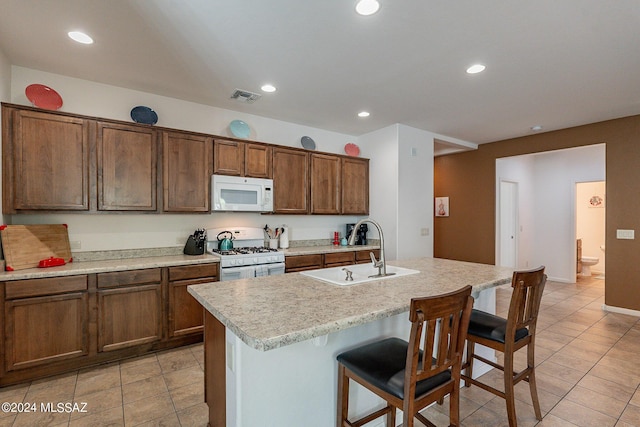 kitchen featuring light tile patterned flooring, a breakfast bar, an island with sink, sink, and white appliances