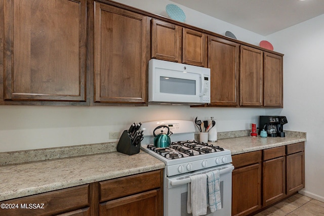 kitchen featuring light stone counters, light tile patterned floors, and white appliances