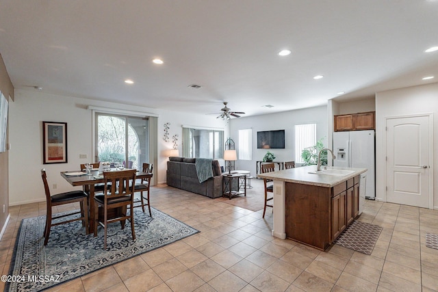 kitchen featuring a sink, white refrigerator with ice dispenser, a kitchen island with sink, light countertops, and recessed lighting