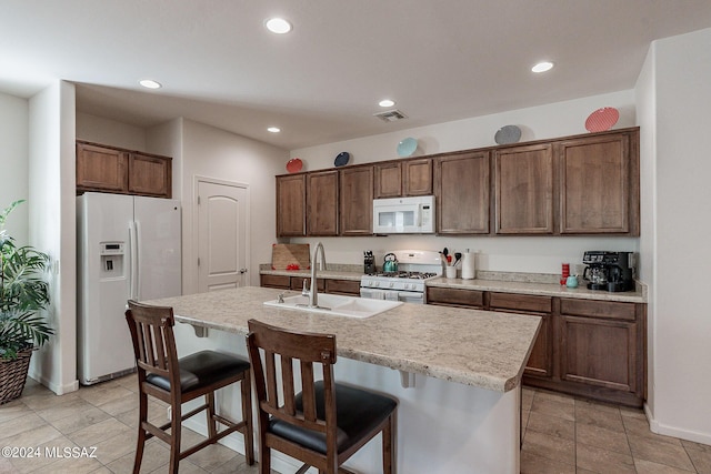 kitchen with an island with sink, sink, a kitchen breakfast bar, dark brown cabinets, and white appliances