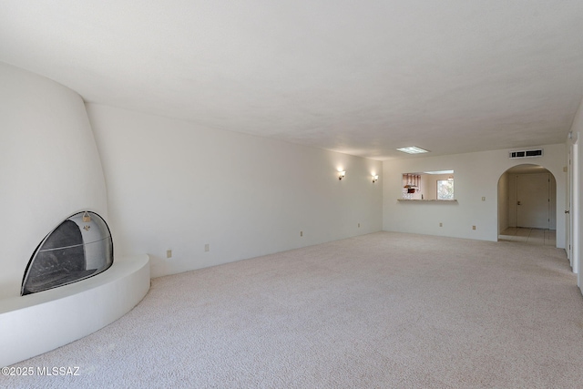 carpeted empty room featuring visible vents and arched walkways