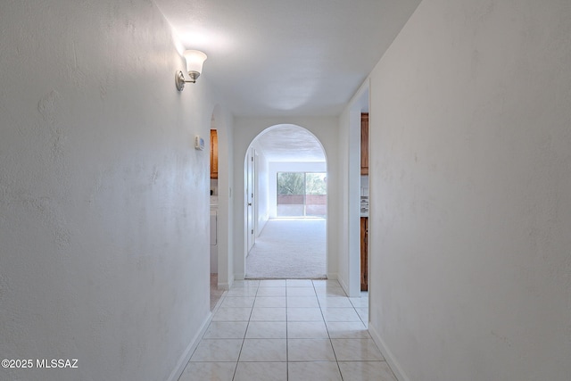 corridor with arched walkways, baseboards, and light tile patterned floors