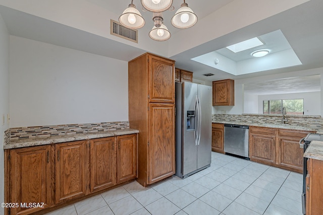 kitchen with a skylight, sink, a raised ceiling, backsplash, and appliances with stainless steel finishes