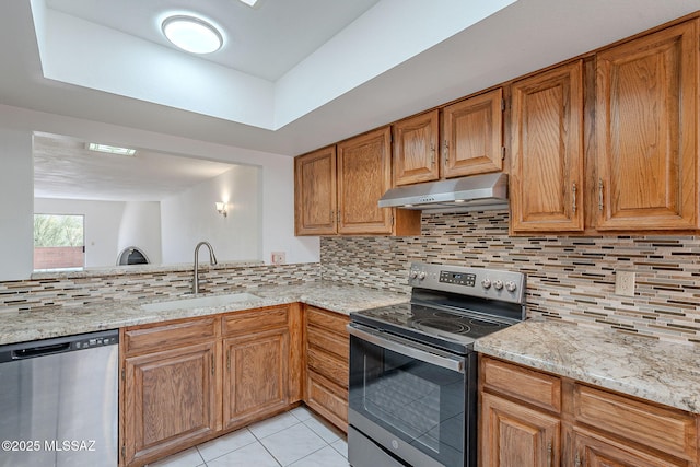 kitchen with light tile patterned flooring, under cabinet range hood, a sink, appliances with stainless steel finishes, and tasteful backsplash